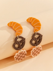 Macro detail of acrylic food-shaped earrings with croissant and pretzel design elements