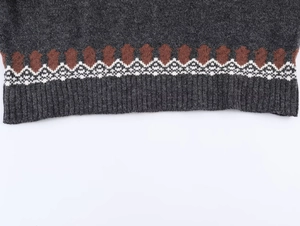 Detail of dark grey knit sweater hem featuring geometric jacquard pattern and ribbed cuff