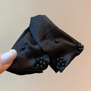 Close-up of black satin hair scrunchie with beaded flower detail and subtle glitter