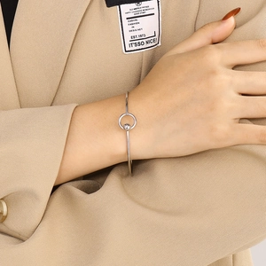 Detail of silver minimalist open bangle with ring and bead charm worn by a model