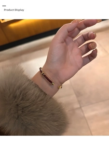 Dettaglio del bracciale in pelle intrecciata rossa con decorazione metallica dorata a X
