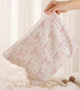 Detail showing the textured rib fabric with pink bows and hearts on a beige cosmetic bag