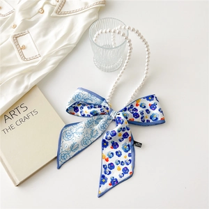 Detail of pearl strap handle with blue floral silk scarf tied in a bow on white desk