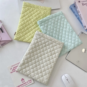 Quilted diamond laptop sleeves in pastel green, blue, and cream on a desk