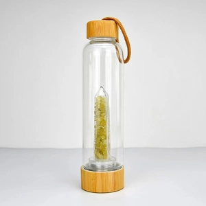 Close-up of glass energy bottle with yellow crystal pillar, gravel and bamboo lid
