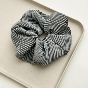 Detailed view of grey pleated scrunchie with silky luster on a minimalist beige tray