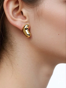 Detail of 18k gold plated bean-shaped stud earrings worn by a model on a light background