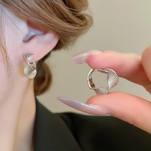 Macro detail of silver twisted hoop earrings with textured finish on human ear
