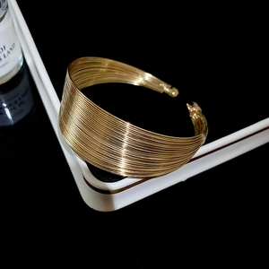Macro view of a gold multi-layer wire cuff bracelet on a white display pedestal