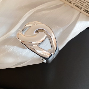 Detailed close-up of a high-polished silver crossover ring on white pleated fabric