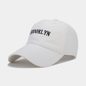 Close-up of white cotton baseball cap featuring black Brooklyn embroidery and curved brim