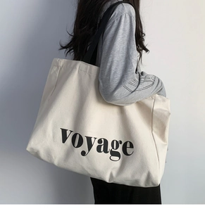 Minimalist cream canvas tote bag with black voyage lettering shown on a female model