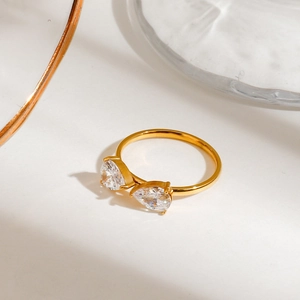Close-up of golden stainless steel ring with two pear-cut zircons on a white surface