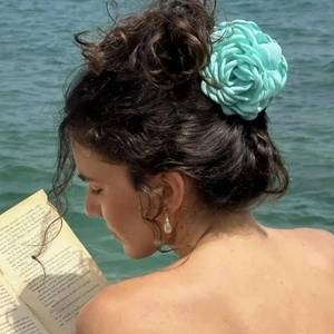 Detail of mint green fabric flower hair claw worn by a model in a coastal setting