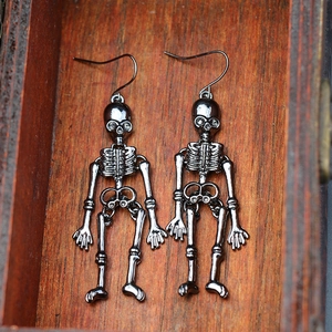 Close-up of black metal skull earrings presented inside a textured wooden jewelry box