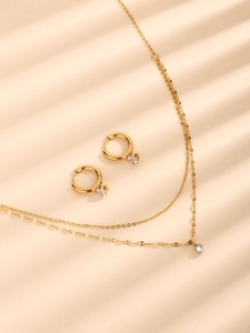 Detail of gold double-layer necklace and matching stud earrings with clear gemstones