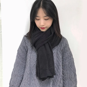 Detail of a black knit scarf showing fine texture and drape on a grey cable sweater