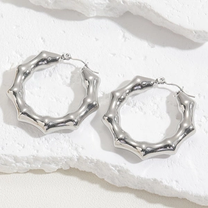 Macro shot of silver bamboo textured hoop earrings on a white textured stone surface