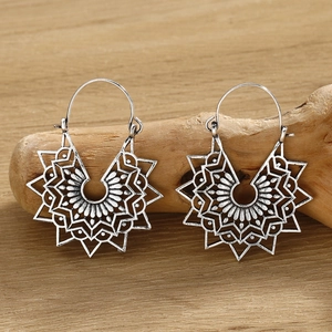 Detailed silver mandala earrings with hollow star pattern on a textured wood surface