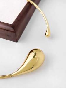Macro detail of high-polish gold teardrop choker with smooth mirror metallic finish