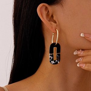 Close-up of geometric acrylic earrings with black and marble textures on a female model