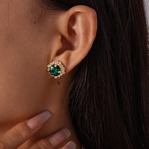 Close-up of elegant emerald green stud earrings with shimmering diamond halo on model