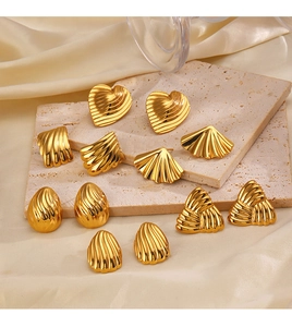 Close-up of golden geometric earrings with heart and shell designs on silk
