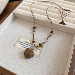 Dettaglio macro del ciondolo a cuore in pietra con cordino intrecciato a mano e perline