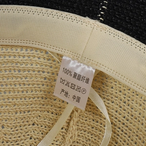 Detail of beige woven sun hat showing 100% polyester label and adjustable inner drawstring