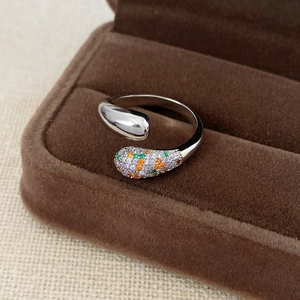 Dettaglio macro di un anello a goccia con zirconi colorati su scatola di velluto