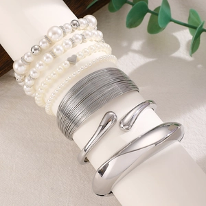 Detail of layered silver metal bangles and white pearl beaded bracelets on a white stand