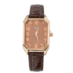 Macro shot of rose gold octagonal watch case with textured brown wood grain dial
