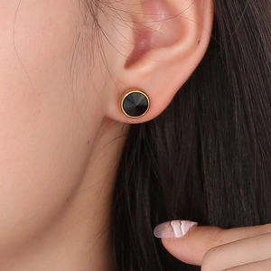 Détail de boucles d'oreilles rondes en pierre noire avec bord doré sur l'oreille