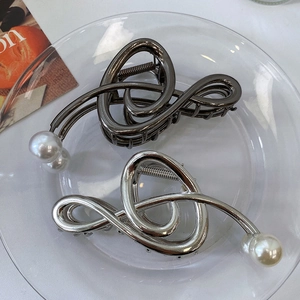 Macro detail of metallic hair claw clips with pearls on a glass tray in 45-degree view