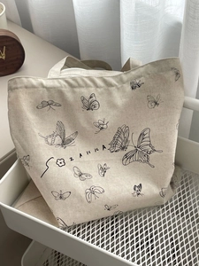Minimalist canvas tote bag with butterfly print and artistic lettering in a white basket