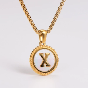 Detailed macro of gold round pendant with white shell inlay and 3D letter X