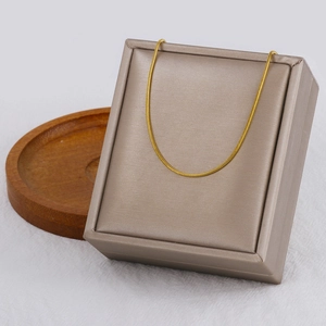 Detail of a thin gold snake chain necklace displayed on a champagne jewelry box