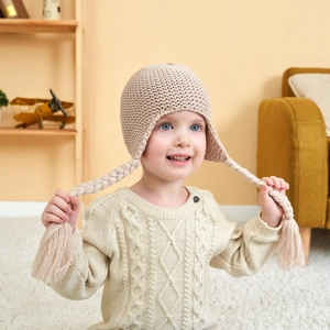 Detail of baby knit hat with braids and tassels against a warm home backdrop