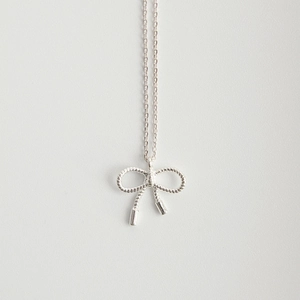 Close-up of minimalist 925 sterling silver bow pendant with fine woven texture