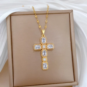 Collier croix élégant en acier titane doré avec zircons dans un écrin à bijoux beige