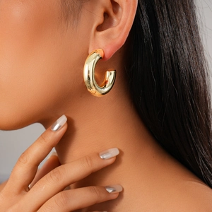 Close-up of a model wearing a thick golden hoop earring with polished metallic finish