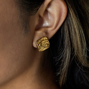 Macro shot of gold stainless steel earrings with textured hammered finish on a model
