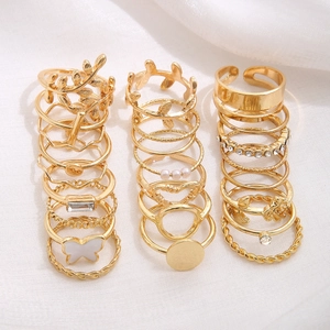 Macro view of 21-piece golden ring set with leaf designs and butterfly charms on white fabric