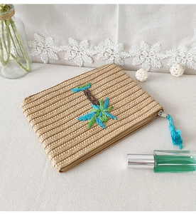 Detail of embroidered palm trees on beige straw clutch with blue tassel zipper