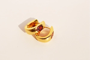 Macro detail of U-shaped gold earrings featuring oval red zircon and polished metal finish