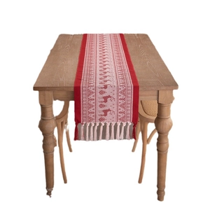 Christmas table runner with red reindeer patterns and beige tassels on a wooden table