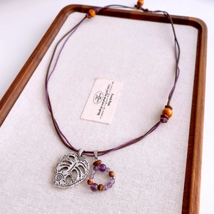 Close-up of vintage hollow leaf pendant with wooden beads and purple crystal on rope cord