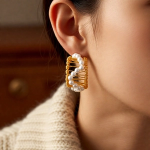 Detailed view of C-shaped 18k gold earrings with pearls on a model's ear