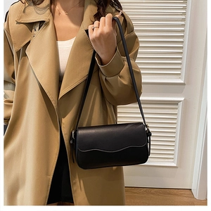 Close-up of a black leather shoulder bag with unique wavy edge flap on a female model