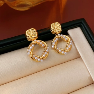 Detail of twisted square gold earrings with small pearls on a beige velvet background